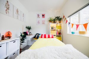 massage treatment room with massage couch, a desk, shelves, indoor plans and and towels.