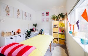massage treatment room with massage couch, a desk, shelves, indoor plans and and towels.