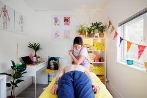 Massage therapist massaging client's back with her elbow in a massage room