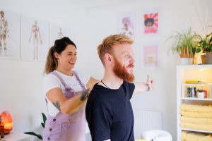 Massage therapist conducting a postural assessment of a male client's shoulder