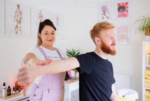 Massage therapist conducting a postural assessment of a male client's shoulder
