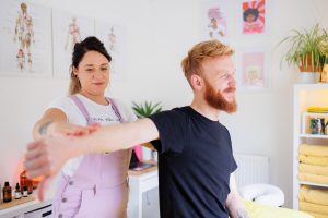 Massage therapist conducting a postural assessment of a male client's shoulder