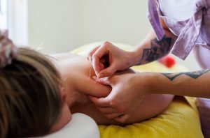 Therapist applying dry needles clients shoulder in a massage room