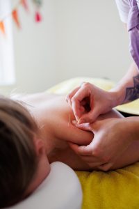 Therapist applying dry needles clients shoulder in a massage room
